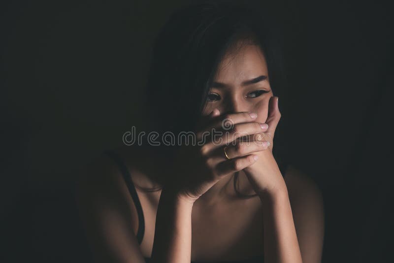 Una donna triste e triste che soffre di vita familiare donne sedute in una stanza buia e toccate il suo volto con preoccupazione immagine stock libera da diritti Una donna triste e triste che soffre di vita familiare donne sedute in una stanza buia e toccate il suo volto con preoccupazione immagine stock libera da diritti