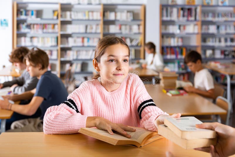 Ten-year-old schoolgirl who came to the school library passes books to the librarian. Ten-year-old schoolgirl who came to the school library passes books to the librarian