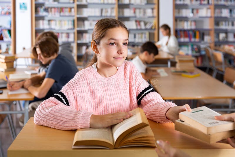 Ten-year-old schoolgirl who came to the school library passes books to the librarian. Ten-year-old schoolgirl who came to the school library passes books to the librarian