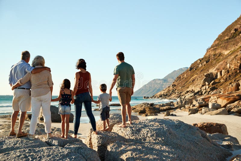 Una famiglia bianca di tre generazioni su una spiaggia sta tenentesi per mano, vista piena d'ammirazione, vista integrale e poste