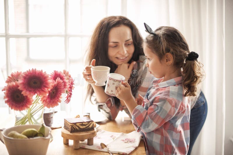 Una familia feliz está desayunando en casa al lado de la ventana en la tabla Flores y café Mama e hija Copie el espacio imagen de archivo libre de regalías Una familia feliz está desayunando en casa al lado de la ventana en la tabla Flores y café Mama e hija Copie el espacio imagen de archivo libre de regalías