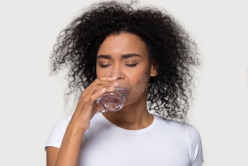 Thirsty young African American woman drinking clean mineral water, attractive female holding glass, healthy lifestyle concept, natural beauty, perfect skin,  on studio background. Thirsty young African American woman drinking clean mineral water, attractive female holding glass, healthy lifestyle concept, natural beauty, perfect skin,  on studio background