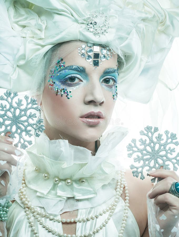 Una giovane bellissima donna con trucco creativo in stile nuovo anno tiene in mano dei fiocchi di neve d'argento vicino al suo vol immagine stock libera da diritti