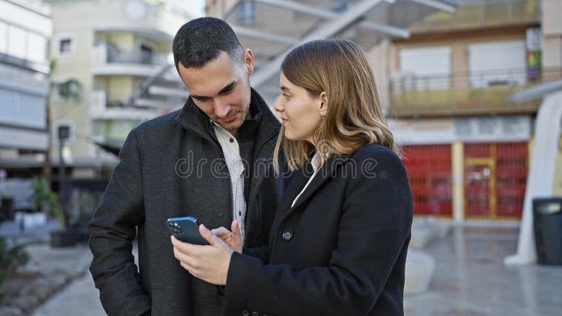 Una giovane coppia di vetri di uno smartphone messi insieme sul marciapiede della città durante una passeggiata informale all'aper immagini stock libere da diritti