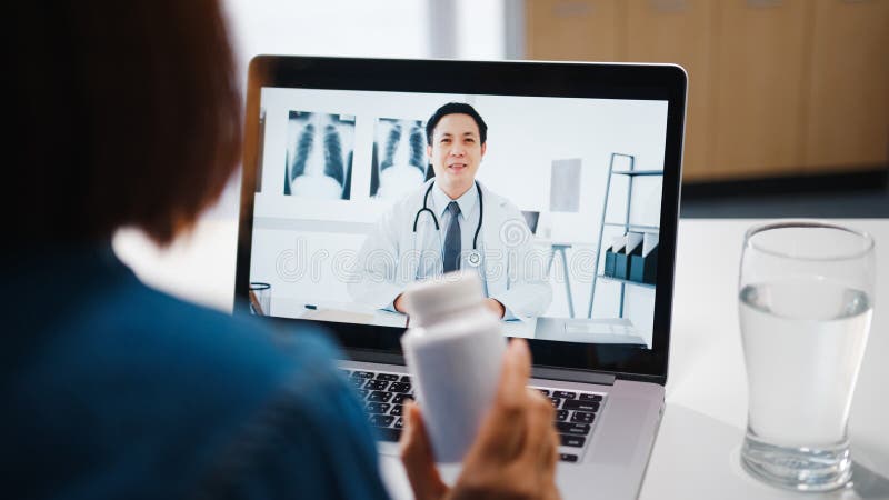 Una giovane donna asiatica che usa un computer portatile parla di una malattia in videoconferenza con un medico senior online all'
