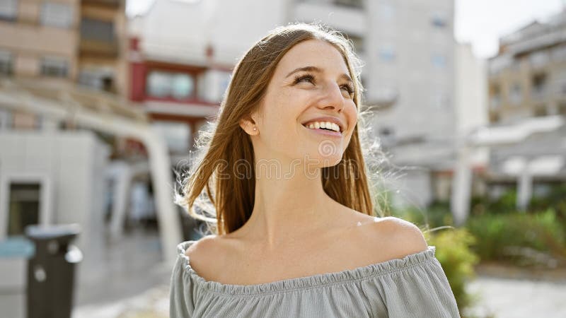 Una giovane donna bionda con i capelli biondi che si gode una giornata di sole in una strada di città che rappresenta la felicità fotografia stock