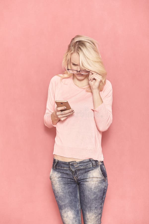 Una giovane donna che guarda al suo Smart Phone con i suoi occhiali, immagini stock libere da diritti Una giovane donna che guarda al suo Smart Phone con i suoi occhiali, immagini stock libere da diritti