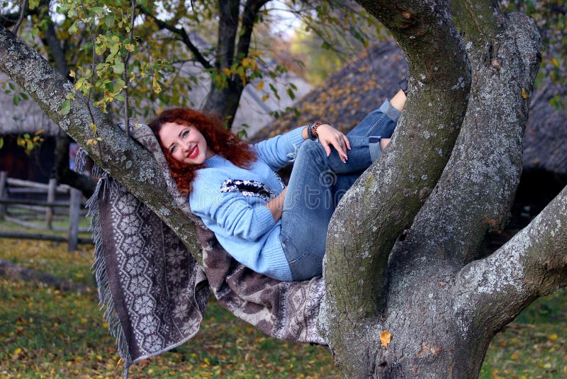 Una giovane donna con capelli rossi e un bello sorriso sta trovandosi su una coperta che è spanta su un albero I sorrisi e esamin fotografie stock Una giovane donna con capelli rossi e un bello sorriso sta trovandosi su una coperta che è spanta su un albero I sorrisi e esamin fotografie stock