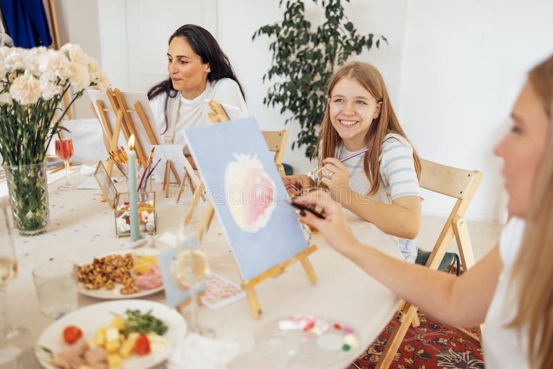 Una giovane donna concentrata con una maglietta bianca e un grembiule dipinge un'immagine a un tavolo e un alluce fotografia stock libera da diritti