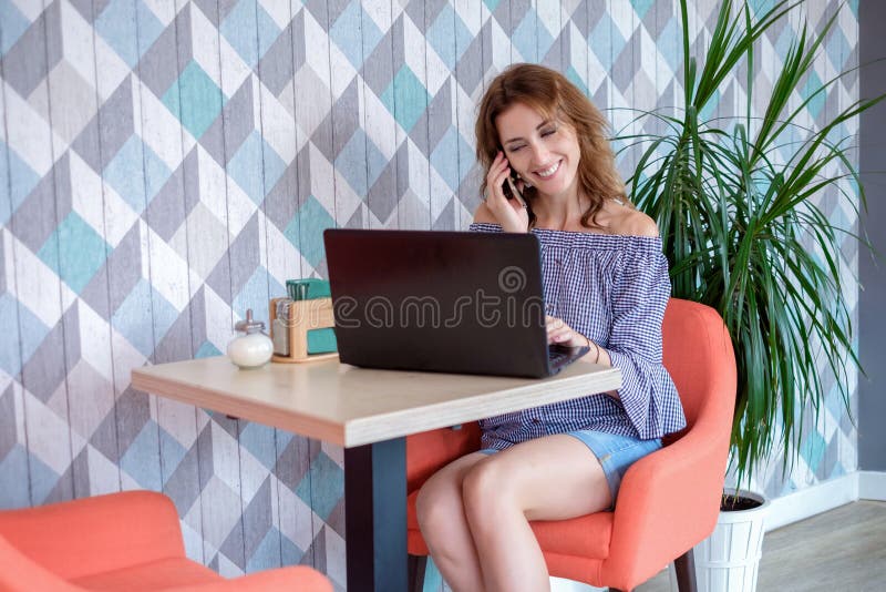 Una giovane donna di affari attraente che per mezzo del suoi telefono e computer portatile ad un caffè fotografie stock Una giovane donna di affari attraente che per mezzo del suoi telefono e computer portatile ad un caffè fotografie stock