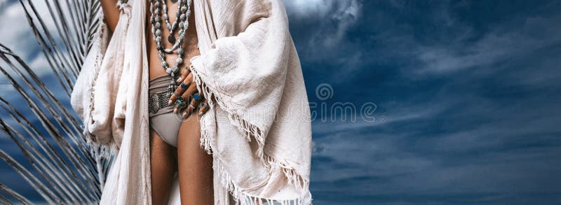 Una giovane donna elegante e di moda con una pelle abbronzata con accessori di boho eleganti sullo sfondo blu del cielo immagini stock