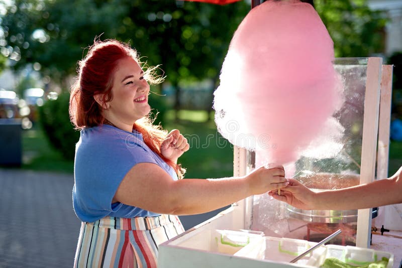 Una giovane donna grassa compra caramella di cotone su un bastone fotografia stock Una giovane donna grassa compra caramella di cotone su un bastone fotografia stock