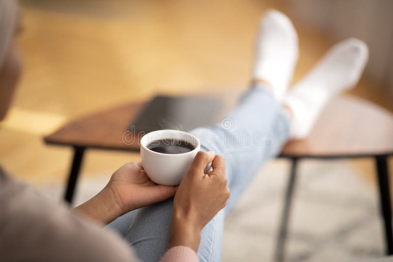 Una giovane donna nera che si riscalda le mani su una tazza di caffè rilassante in casa, spazio vuoto immagini stock