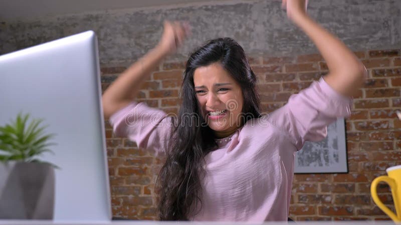 Una giovane ragazza occupata lavora nell'ufficio del sottotetto su un computer portatile, stampa, si rallegra nella vittoria, la