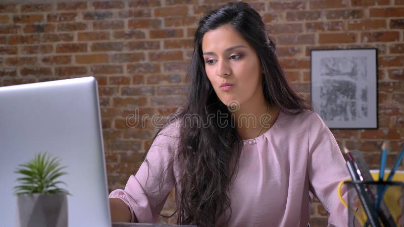 Una giovane ragazza occupata sta lavorando nell'ufficio del sottotetto su un computer portatile, scrivendo, caffè bevente, prende