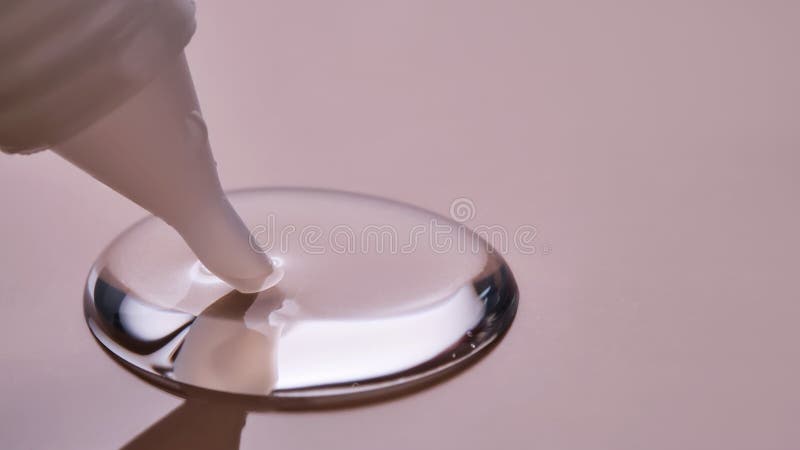 A drop of cosmetic product pours from a tube onto a pink background. High quality photo. A drop of cosmetic product pours from a tube onto a pink background. High quality photo.