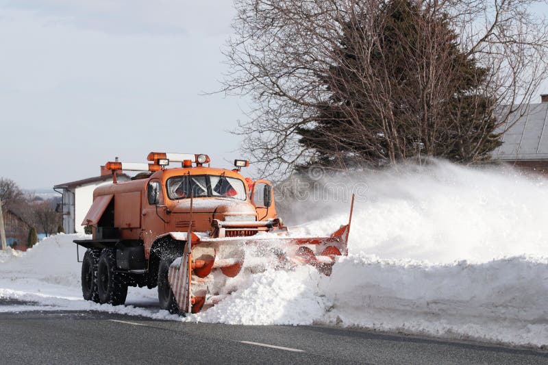 Una grande automobile con un aratro rimuove la strada da neve L'attrezzatura speciale del carico arancio sta lottando con gli ele immagine stock Una grande automobile con un aratro rimuove la strada da neve L'attrezzatura speciale del carico arancio sta lottando con gli ele immagine stock
