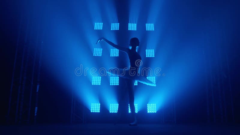 Una graziosa ballerina di silhouette che fa un allenamento in classe. fumo nei raggi di luce blu. ballerino in bianco
