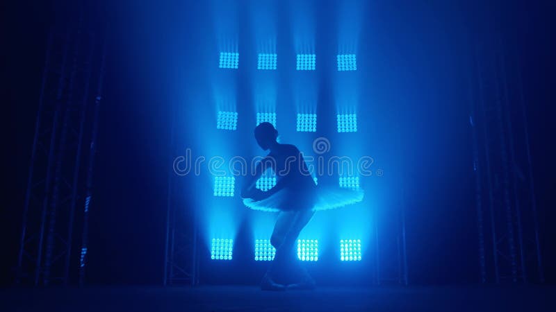 Una graziosa ballerina di silhouette che fa un allenamento in classe. fumo nei raggi di luce blu. ballerino in bianco