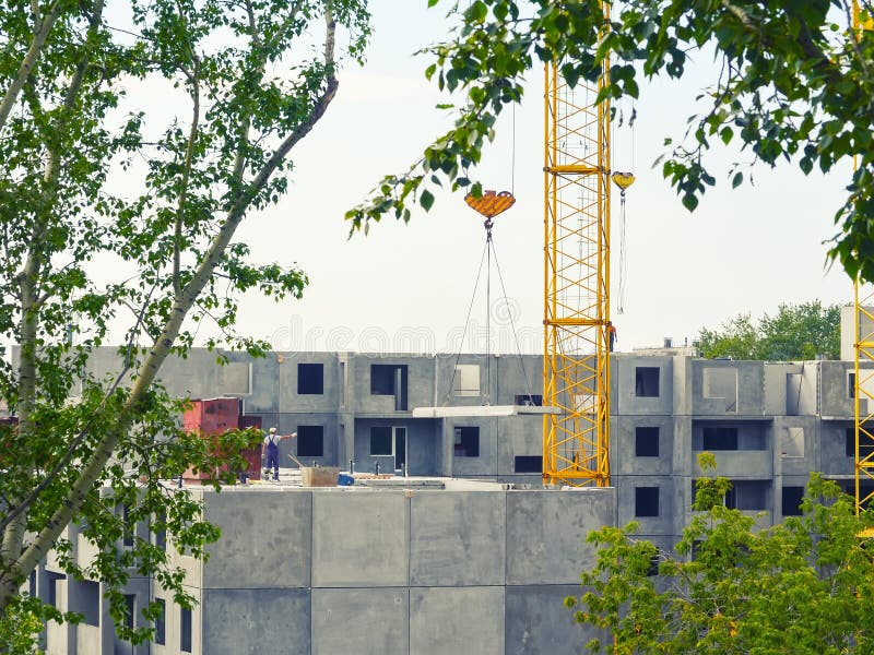Una grúa amarilla levanta un panel concreto en un edificio residencial Un trabajador sin un casco - una violación de normas de se fotografía de archivo Una grúa amarilla levanta un panel concreto en un edificio residencial Un trabajador sin un casco - una violación de normas de se fotografía de archivo
