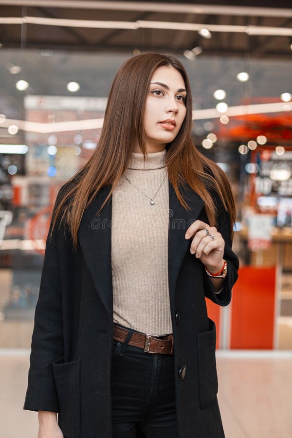 Una Guapa Morena De Una Joven Mujer Con Una Camisa Beige De Moda En Un Elegante  Abrigo Negro Posando En Un Moderno Centro Comercia Foto de archivo - Imagen  de alameda, camisa