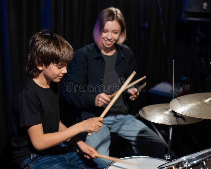 Una joven caucásica enseña a un niño a tocar los tambores en el estudio de fondo negro. estudiante de escuela de música fotos de archivo libres de regalías