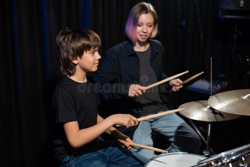 Una joven caucásica enseña a un niño a tocar los tambores en el estudio de fondo negro. estudiante de escuela de música fotos de archivo libres de regalías