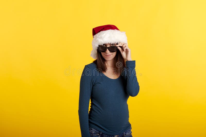 Una joven con gafas de sol con sombrero de Papá Noel y fondo amarillo fotografía de archivo libre de regalías