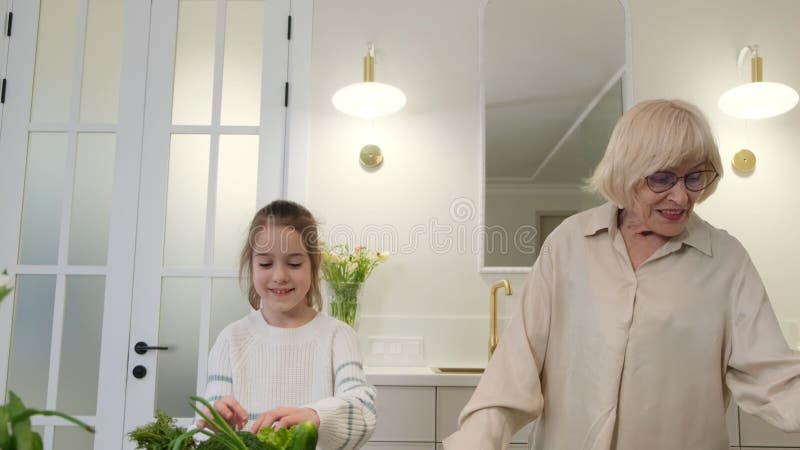 Una joven con un suéter blanco sonríe a su abuela que lleva una blusa beige clara. están de pie en el almacen de metraje de vídeo