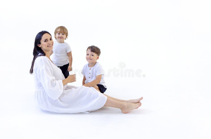 Una joven embarazada con un vestido blanco sonríe y se sienta en el suelo con sus hijos. fondo aislado blanco. riéndose imágenes de archivo libres de regalías