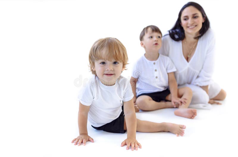 Una joven embarazada con un vestido blanco con sus lindos hijos. mamá adorable y sus pequeños niños están jugando en el suelo. bla imagen de archivo