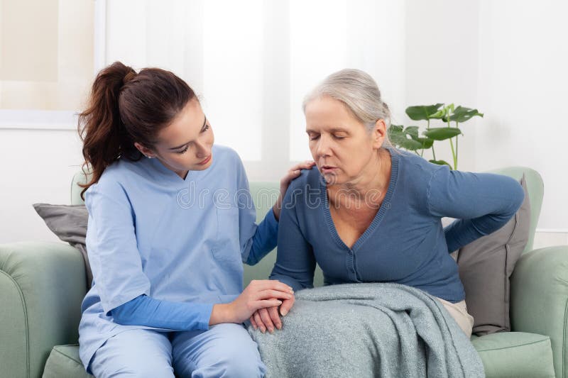 Una joven enfermera o un médico que atiende a una paciente anciana que está estresada y preocupada por el dolor de espalda. atenci imagen de archivo libre de regalías