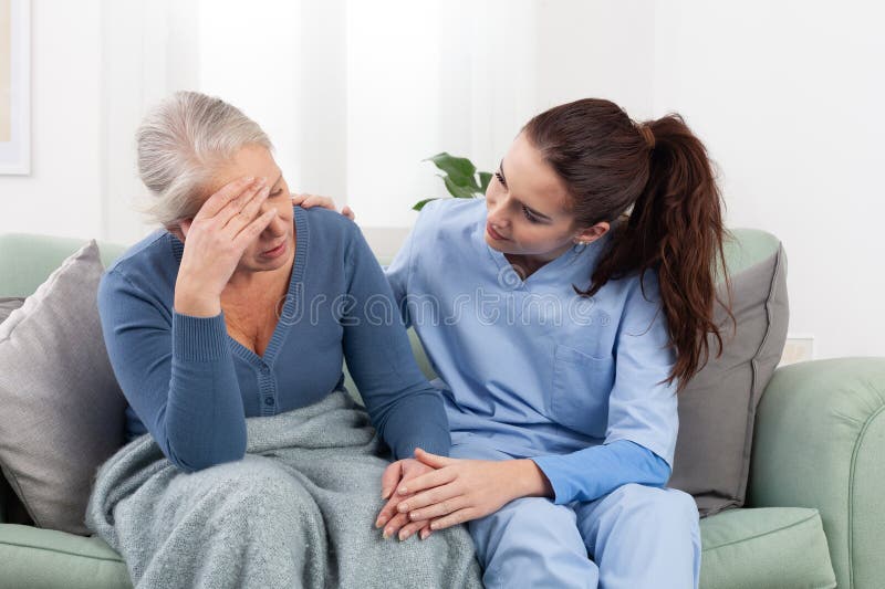 Una joven enfermera o un médico que atiende a una paciente de edad avanzada que está alterada o preocupada por un problema o dolor foto de archivo libre de regalías
