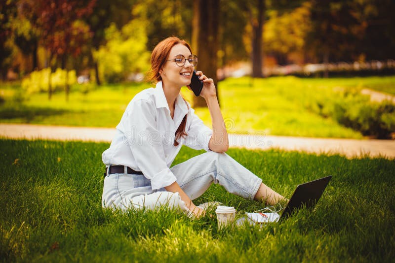 Una joven estudiante trabaja con una laptop al aire libre mientras está sentada en el pasto. educación. comunicar foto de archivo