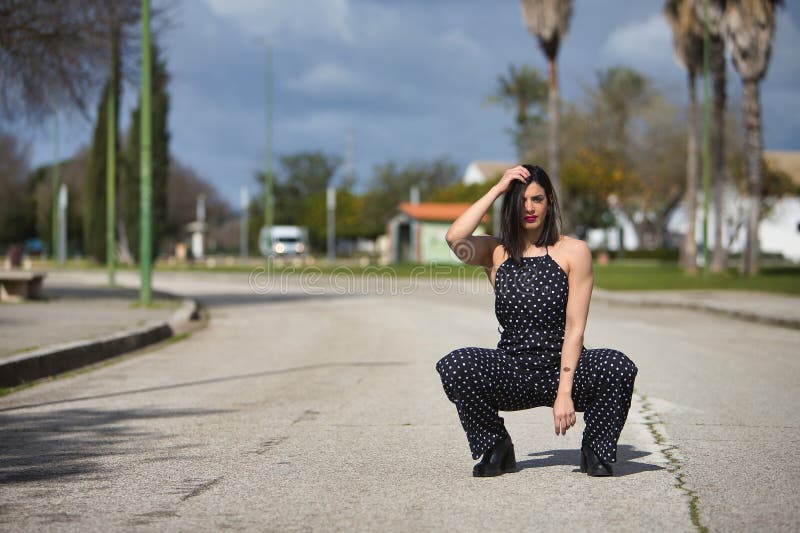 Una joven hermosa mujer con un vestido negro con puntos de polka blanco se agachó triste y sola en medio de un camino. concepto foto de archivo libre de regalías