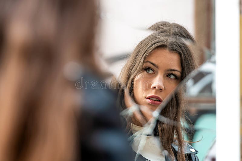 A young, positive woman looks at her reflection in a broken mirror. A young, positive woman looks at her reflection in a broken mirror