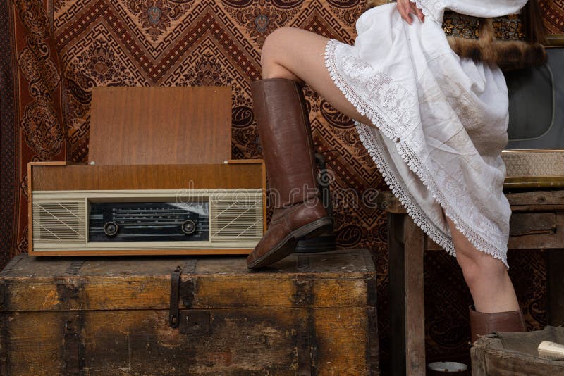Una Joven Mujer Con Blanco Nacional Y Zapatos Viejos De Cuero Su Pierna En El Pecho Cerca De La Vieja Radio Foto de archivo - Imagen encantador, camisa:
