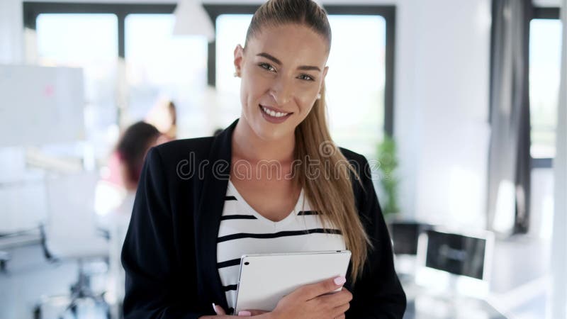 Una joven mujer de negocios rubia mirando su tablet digital mientras sonríe mirando la cámara en la oficina metrajes