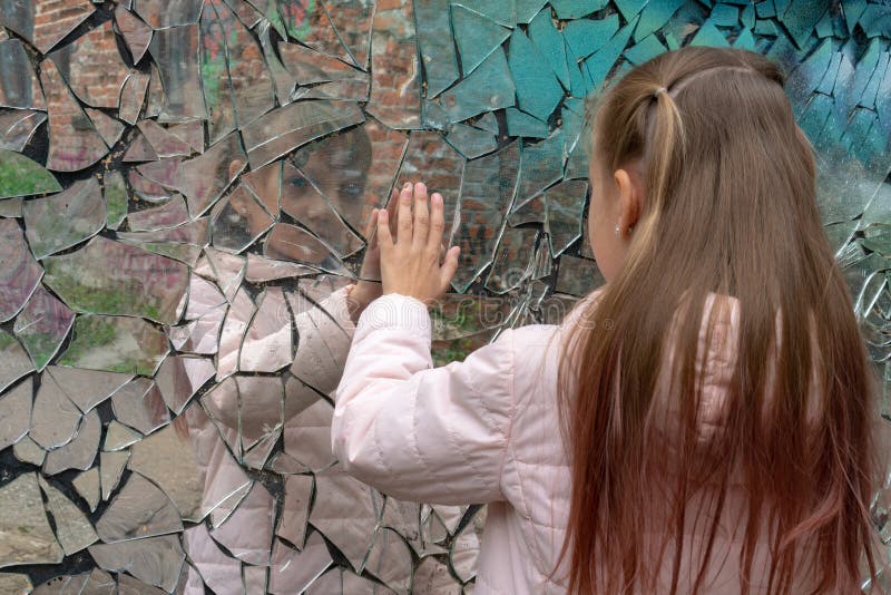 Young girl looks in a broken mirror and shows her hand on a mirror. Young girl looks in a broken mirror and shows her hand on a mirror.