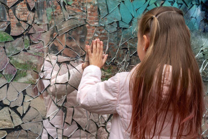 Young girl looks in a broken mirror and shows her hand on a mirror. Young girl looks in a broken mirror and shows her hand on a mirror.