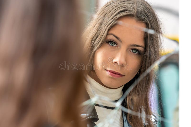 A young, positive woman looks at her reflection in a broken mirror. A young, positive woman looks at her reflection in a broken mirror