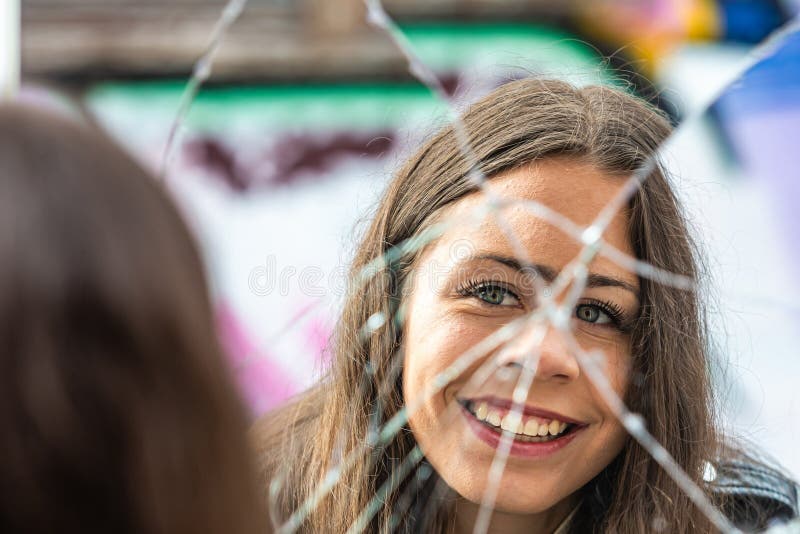 A young, positive woman looks at her reflection in a broken mirror. A young, positive woman looks at her reflection in a broken mirror