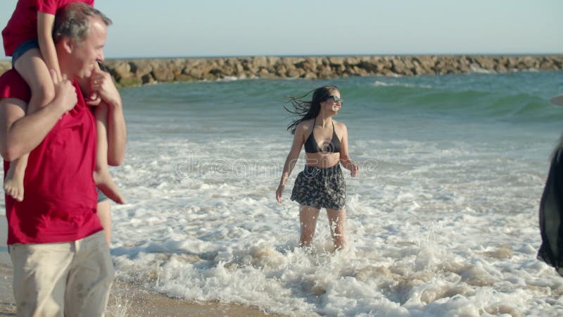 Una lunga fetta di famiglia in piedi sulla spiaggia e spruzzata in mare video d archivio