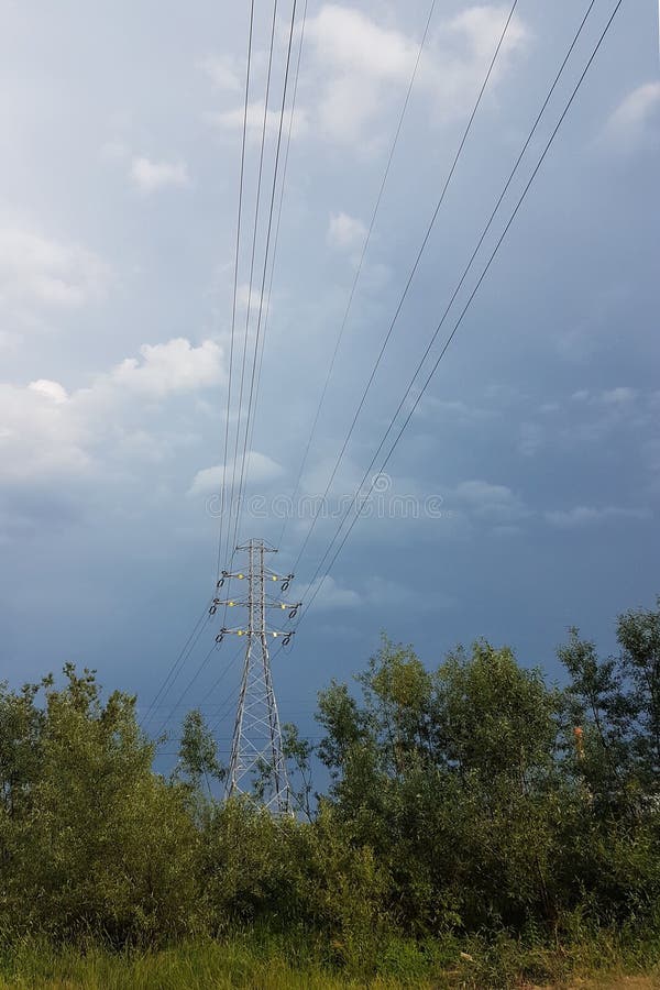 Una línea eléctrica de alto voltaje iluminada por la luz del sol contra un fondo de nubes de un cielo tempestuoso Transporte de l imagenes de archivo Una línea eléctrica de alto voltaje iluminada por la luz del sol contra un fondo de nubes de un cielo tempestuoso Transporte de l imagenes de archivo