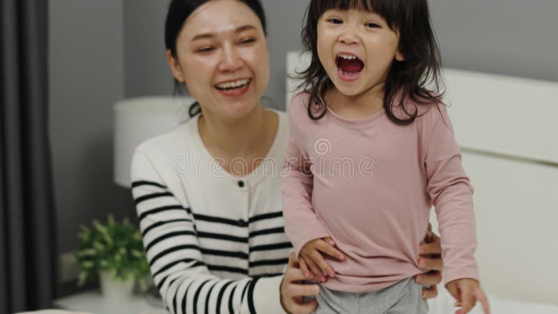 Una madre alegre y una niña pequeña jugando en la cama almacen de video