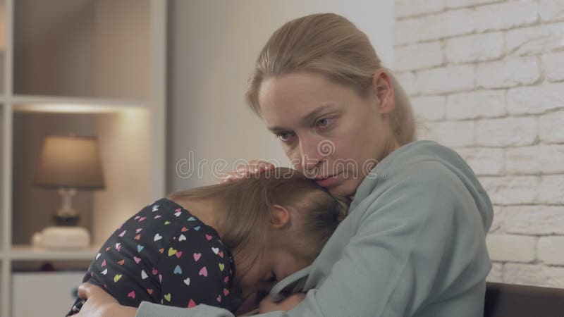 Una madre che abbraccia la figlia che dorme tra le braccia in casa.