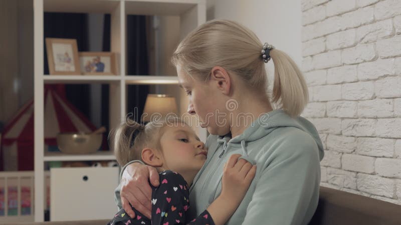 Una madre che abbraccia la figlia che dorme tra le braccia in casa.