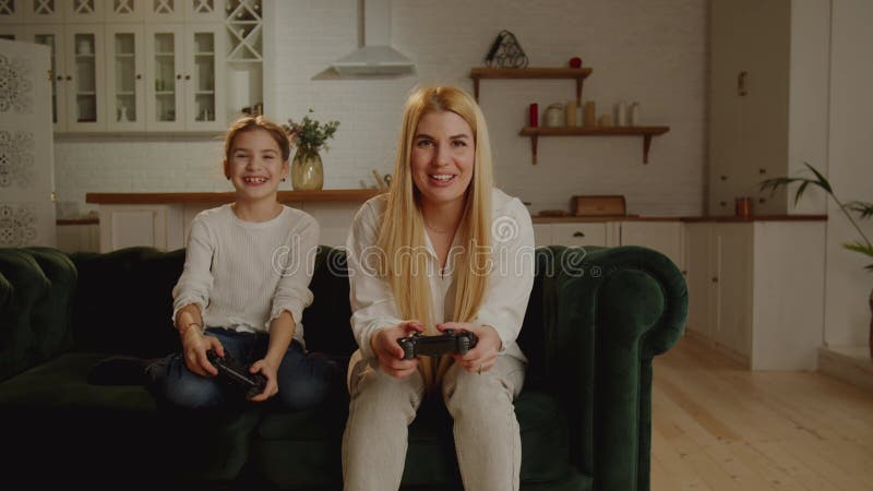Una madre moderna y su hija juegan a juegos de video sentados en un cómodo sofá. el concepto de pasatiempo divertido para los niño almacen de metraje de vídeo