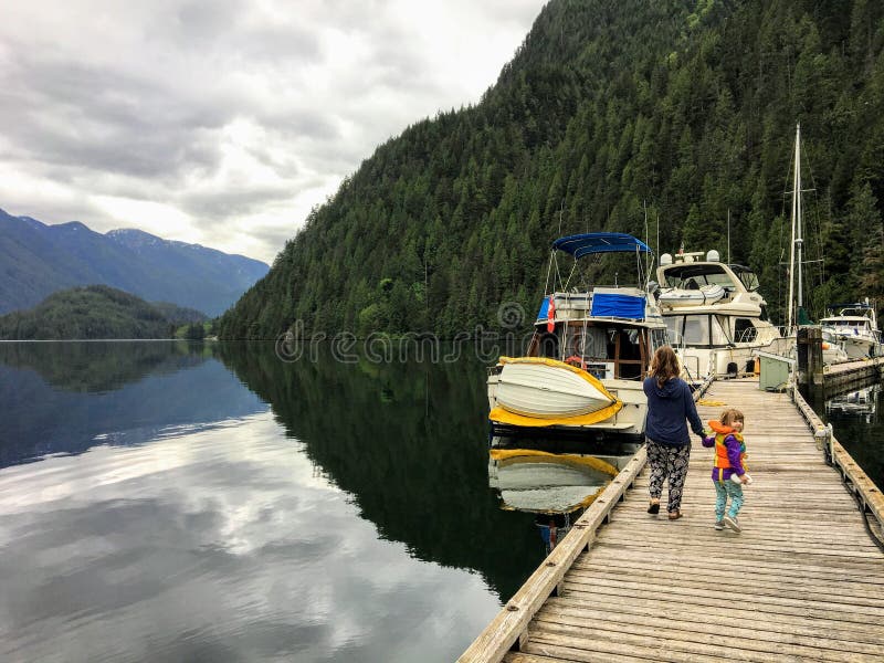 Una madre y su hija de 5 años joven que llevan a cabo las manos que caminan a lo largo del muelle hacia su barco imagen de archivo Una madre y su hija de 5 años joven que llevan a cabo las manos que caminan a lo largo del muelle hacia su barco imagen de archivo