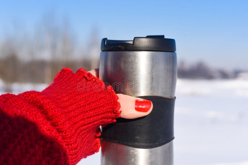 Una mano del ` s della giovane donna in un rosso luminoso ha tricottato il guanto che tiene una tazza di caffè contro i precedent immagine stock libera da diritti Una mano del ` s della giovane donna in un rosso luminoso ha tricottato il guanto che tiene una tazza di caffè contro i precedent immagine stock libera da diritti